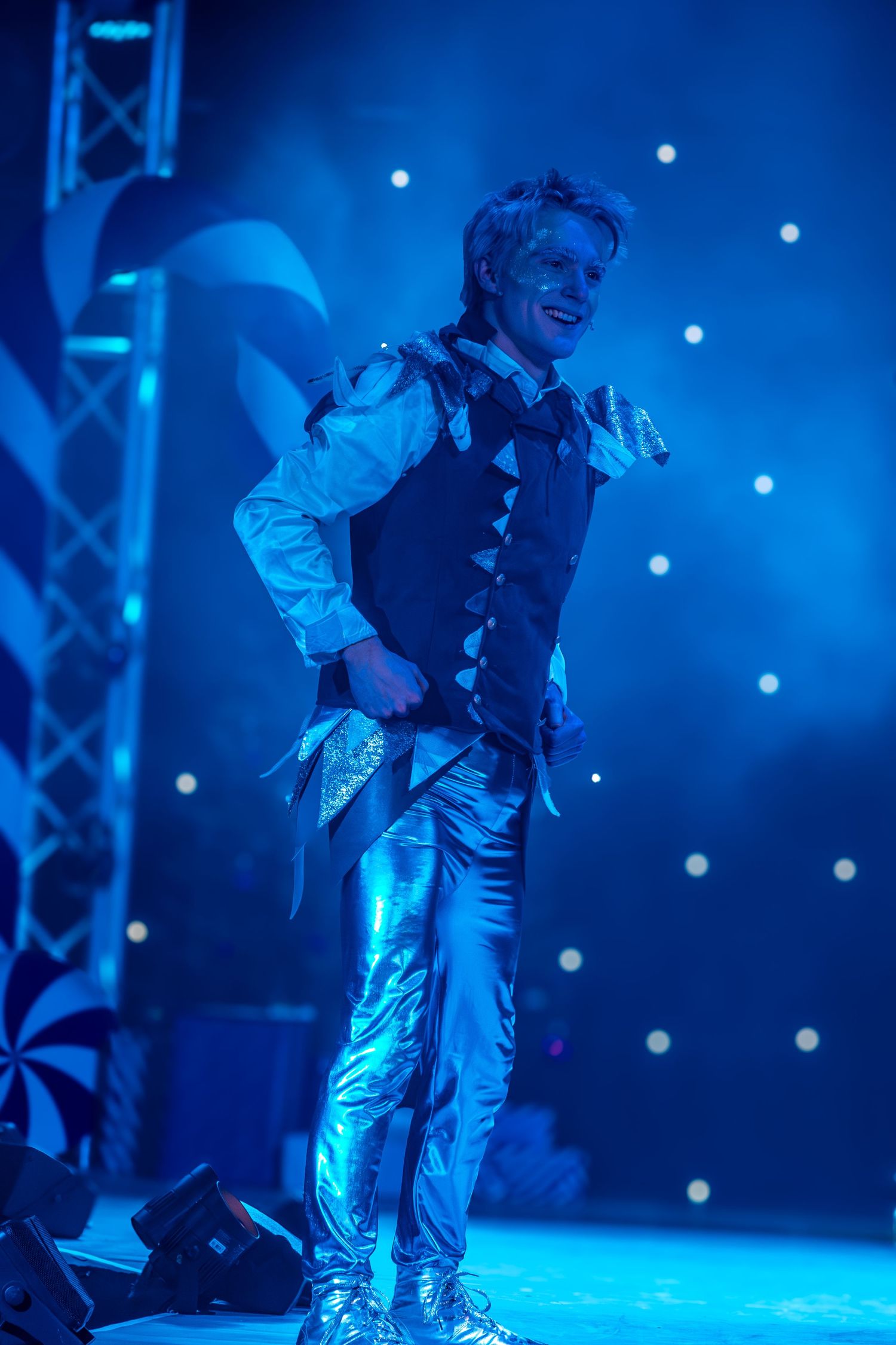 Dancers in silver and black costumes perform under blue spotlights.