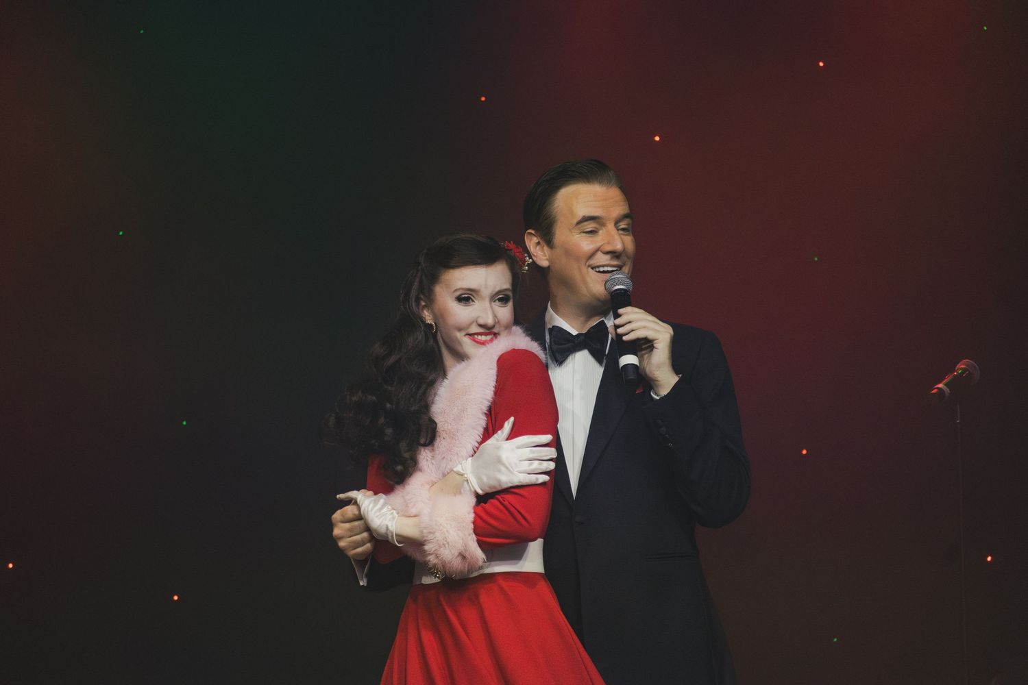 Performers in formal wear share an intimate dance moment on stage.