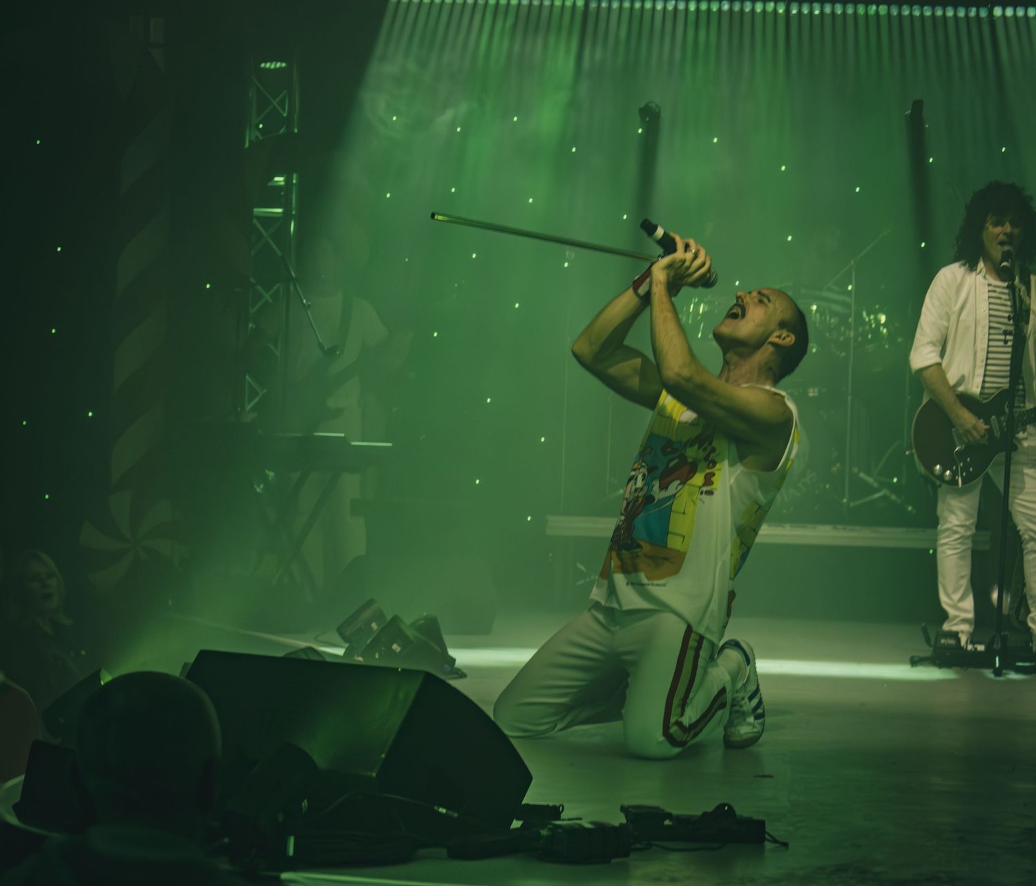 Performers on stage bathed in dramatic green lighting create a theatrical atmosphere during a live show.