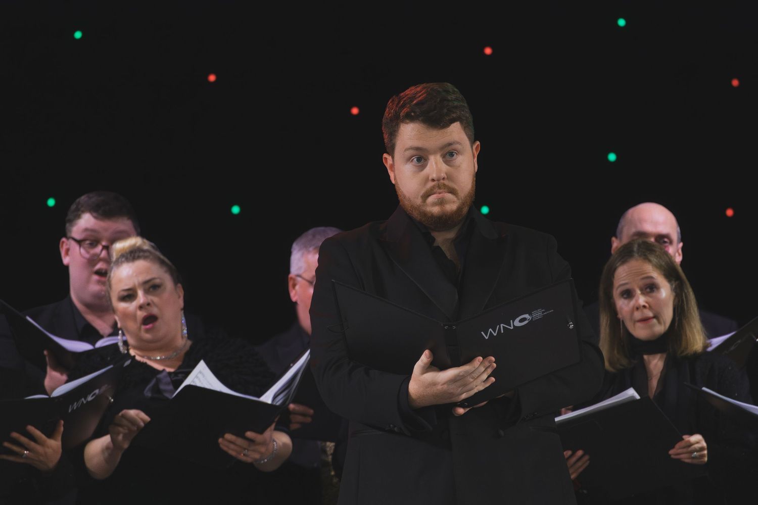 A choir performs on stage with a soloist in black attire standing in front.