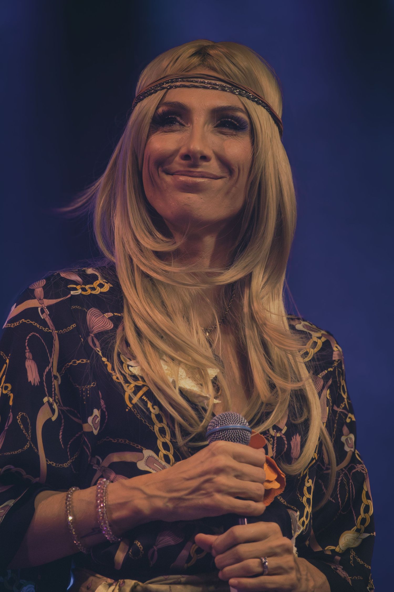 A singer wearing a patterned dress and headband performs under dramatic stage lighting.