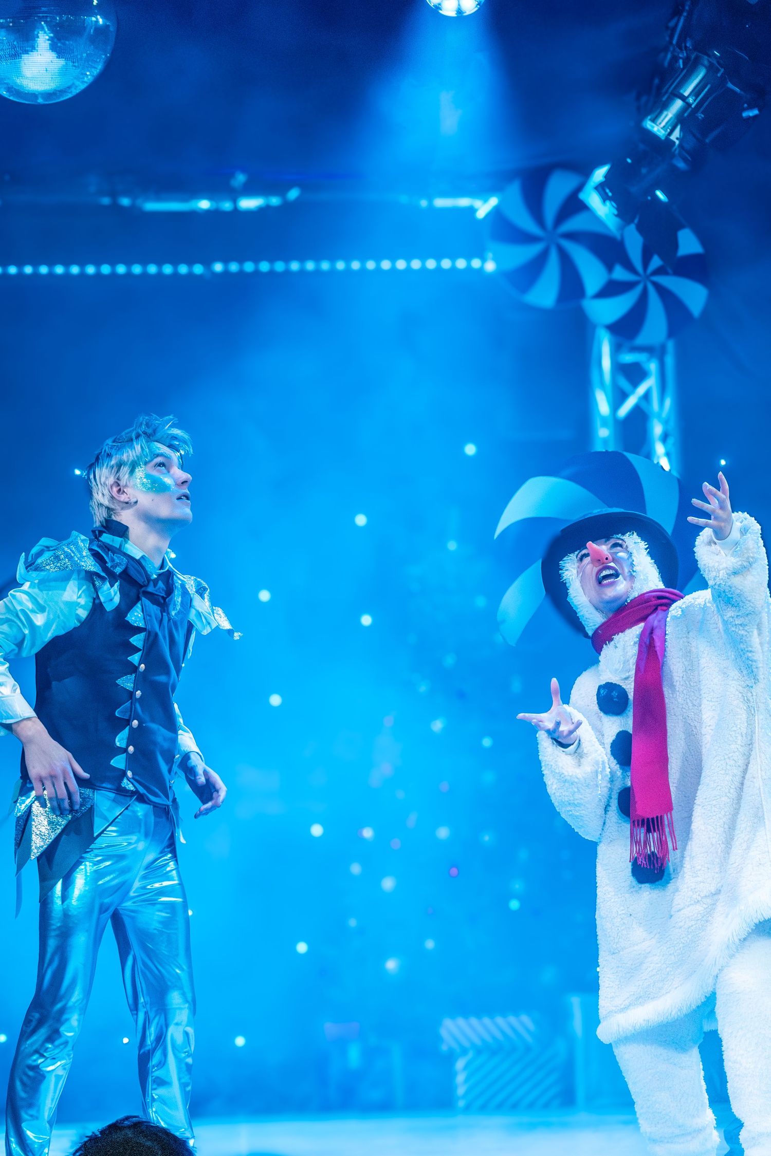 Two performers in contrasting costumes interact during a winter-themed stage show.