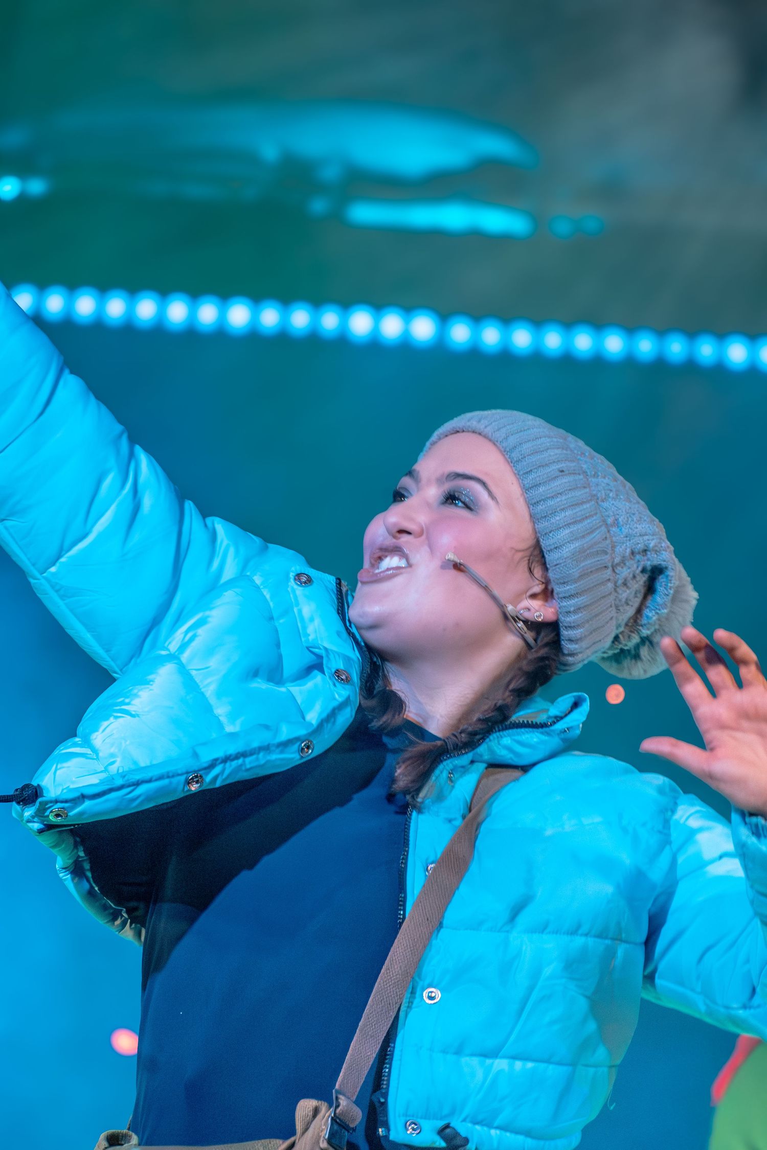 Performer in knit hat singing under dramatic blue stage lighting during an emotional performance.