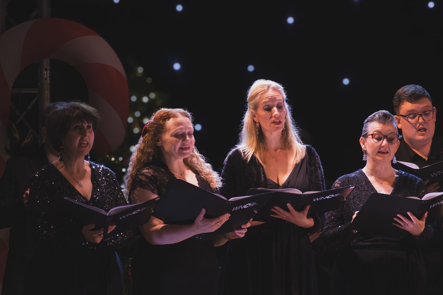 A choir performs on a dark stage with spotlights illuminating the singers as they stand in formation.