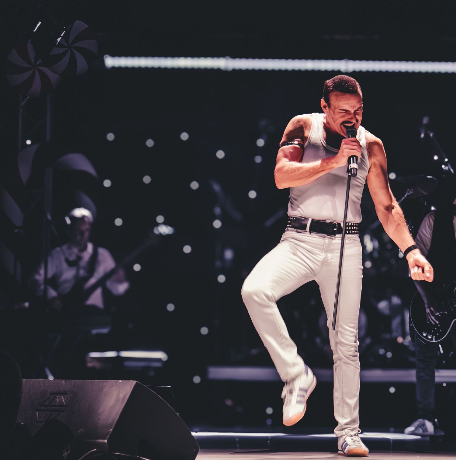 A performer in white clothing energetically sings on stage during a dynamic concert performance.