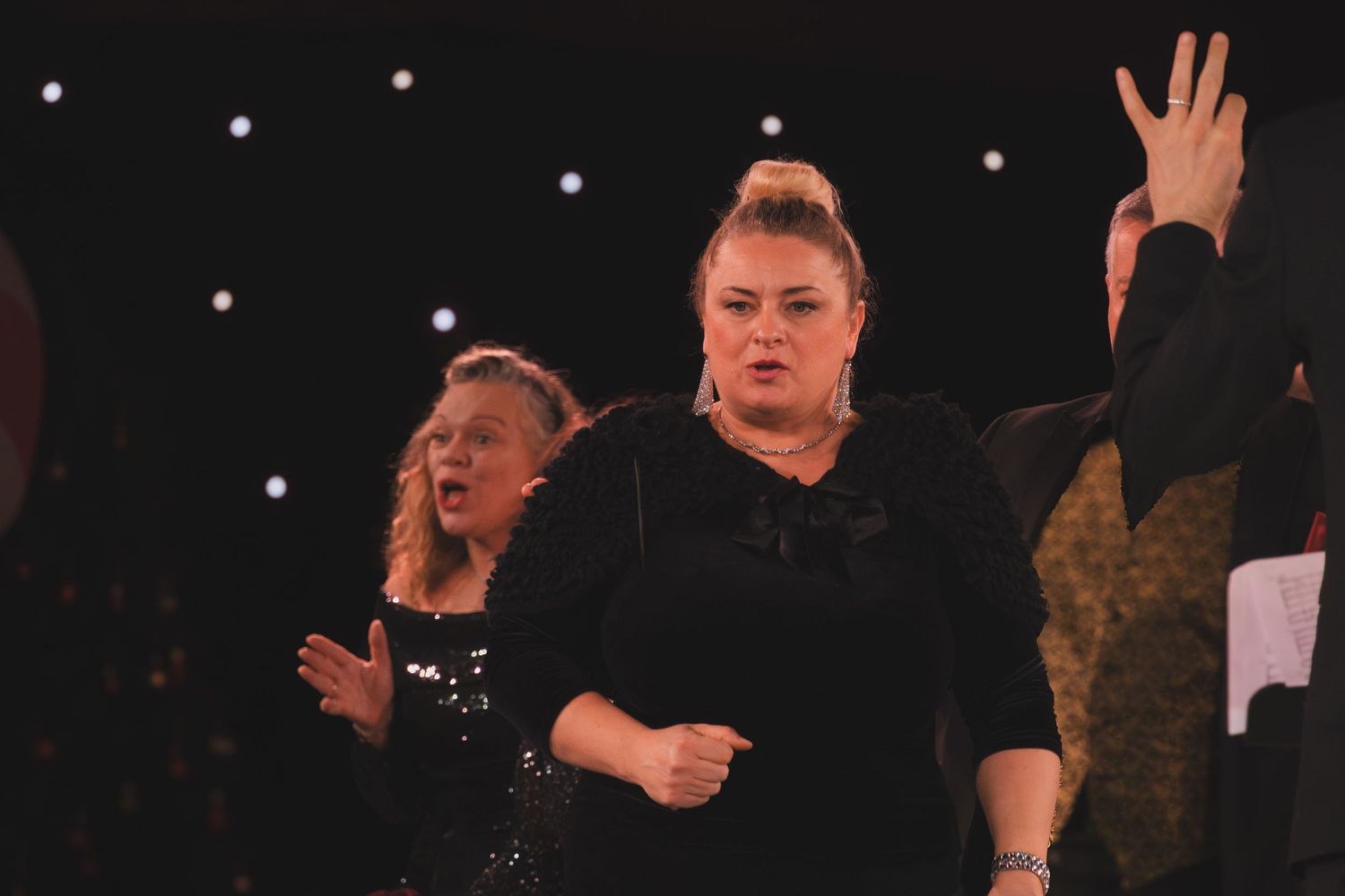 Performers in black attire singing expressively during an emotional musical number.