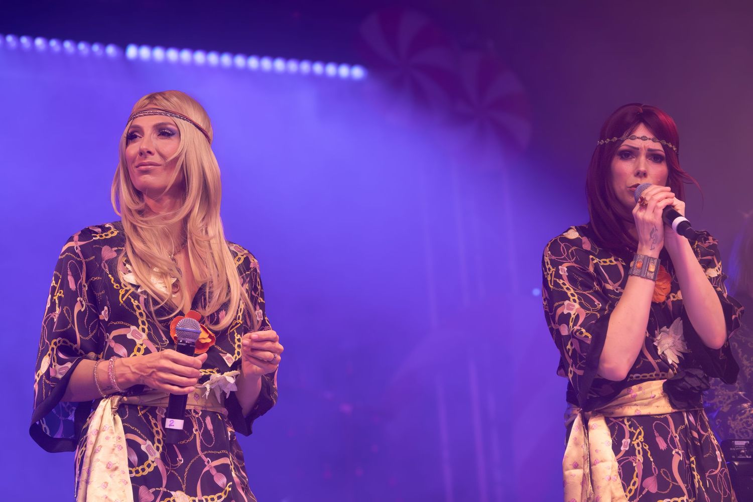 Two performers in matching patterned outfits sing together on stage.