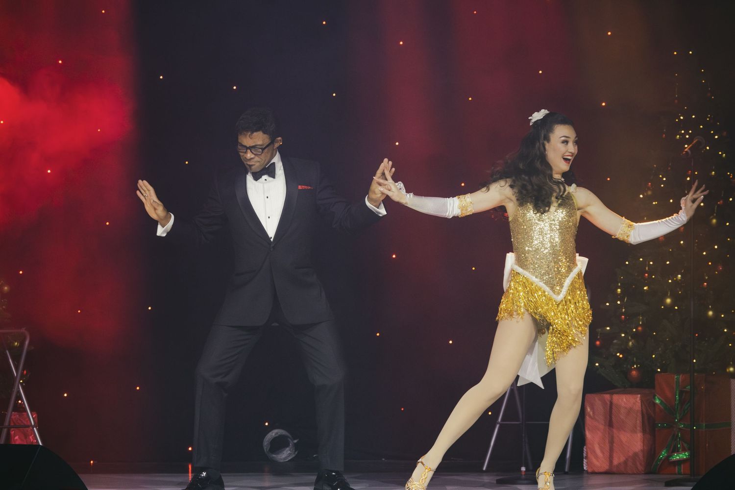 Two performers dance together on stage, one in a tuxedo and one in a gold costume.