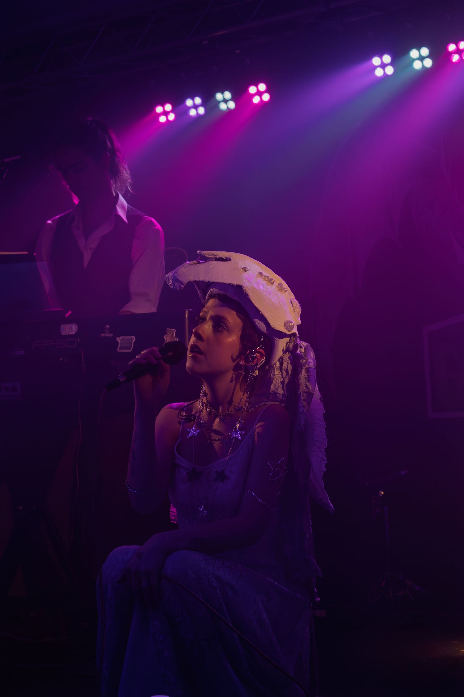 Artist performs on dimly lit stage under vibrant purple stage lighting during an emotional musical performance.
