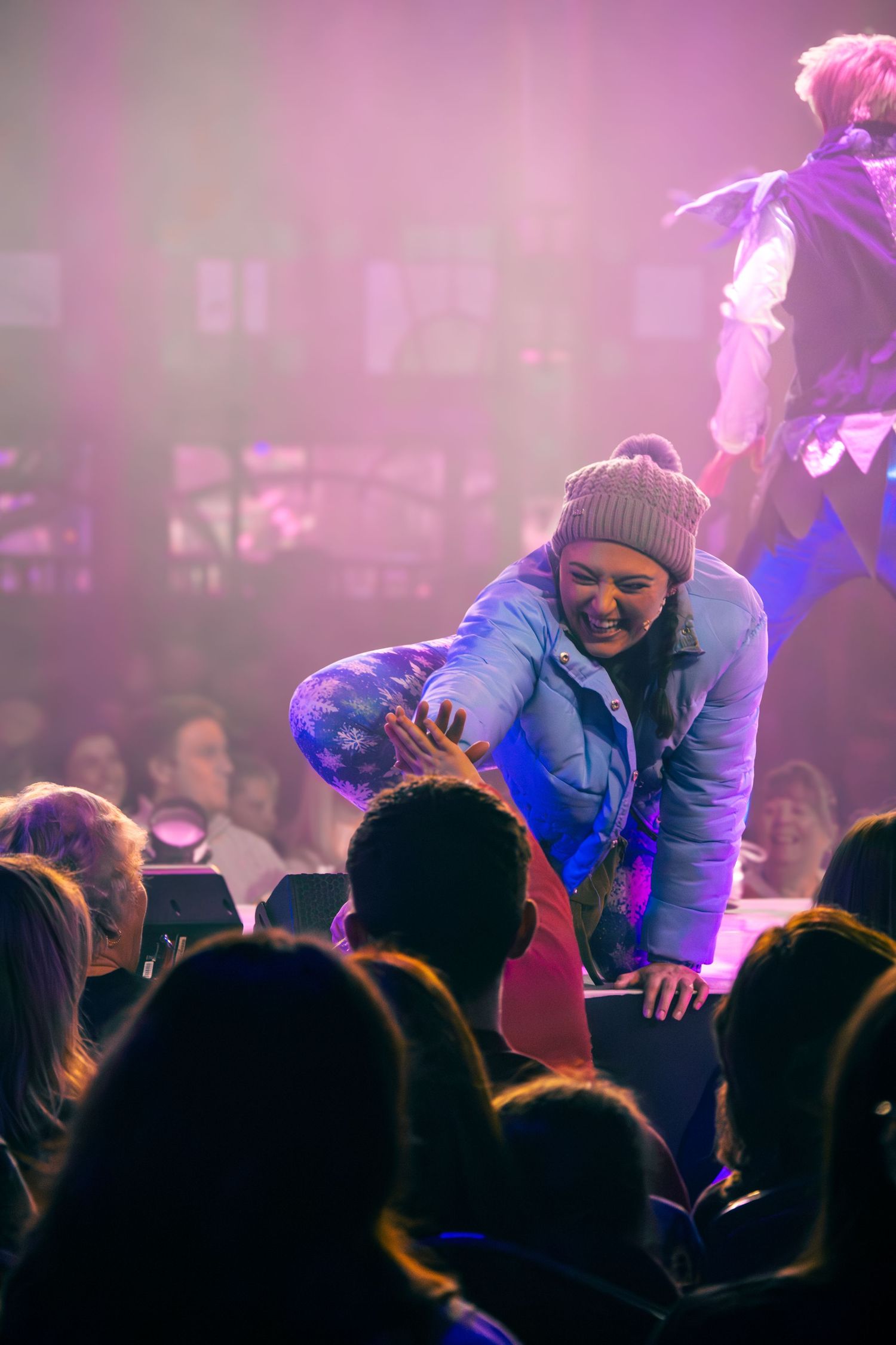 A performer in winter attire interacts with the audience during a live show.