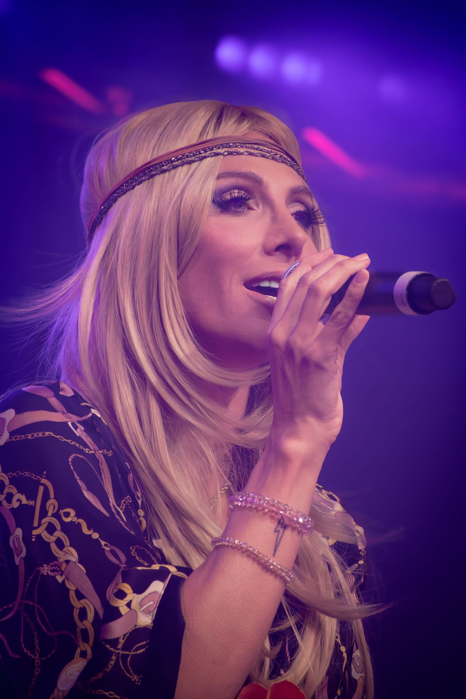 Singer performing on stage with dramatic purple lighting and sparkly outfit.