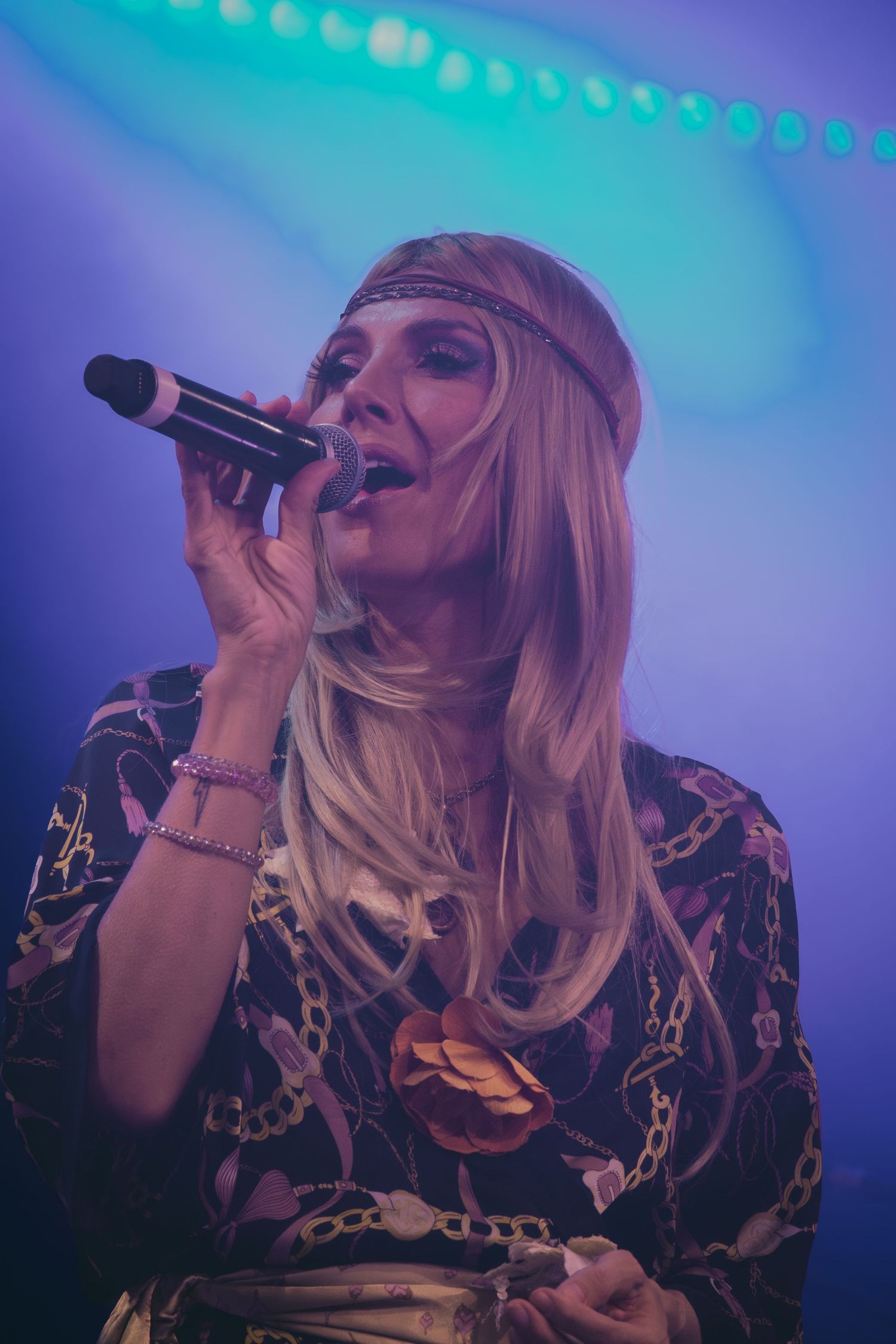 Performer in patterned outfit sings energetically against blue concert lighting.