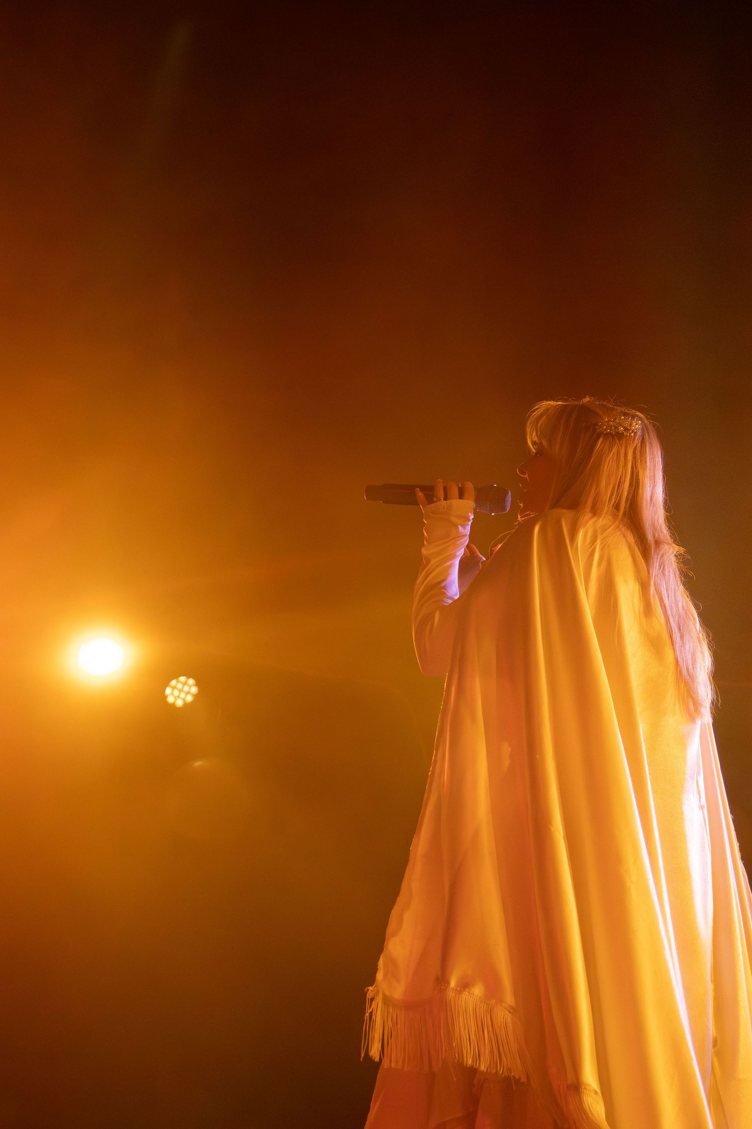 Stage performance silhouetted against warm orange lighting creates ethereal atmosphere.