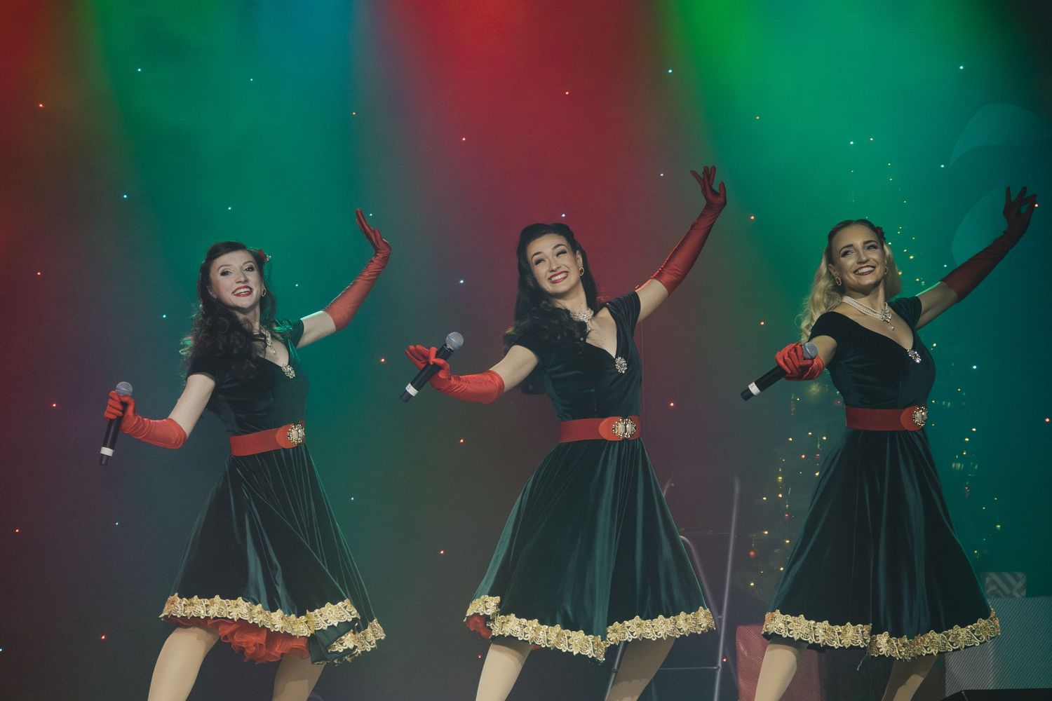 Dancers in green dresses with gold trim perform choreographed routine on stage.