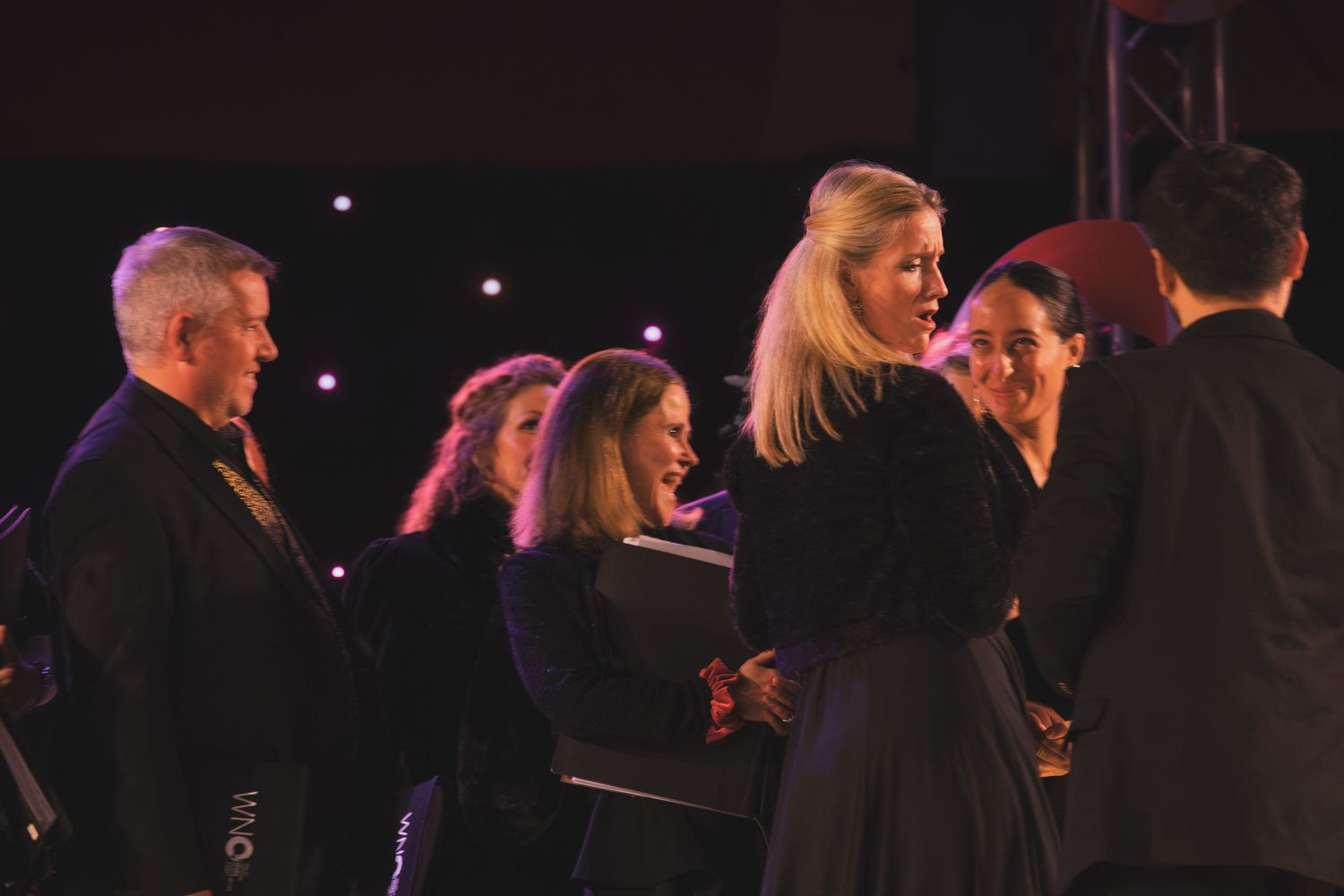 Stage performers arranged in formation during a theatrical production with dramatic lighting effects.