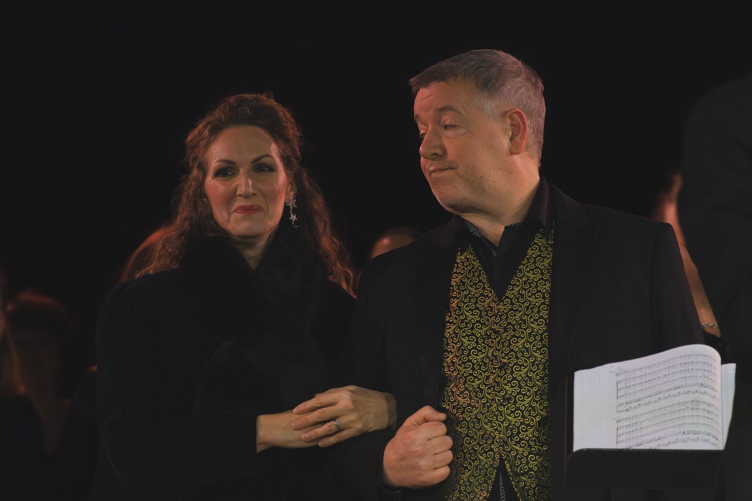 Performers hold scripts while rehearsing on a dimly lit stage.