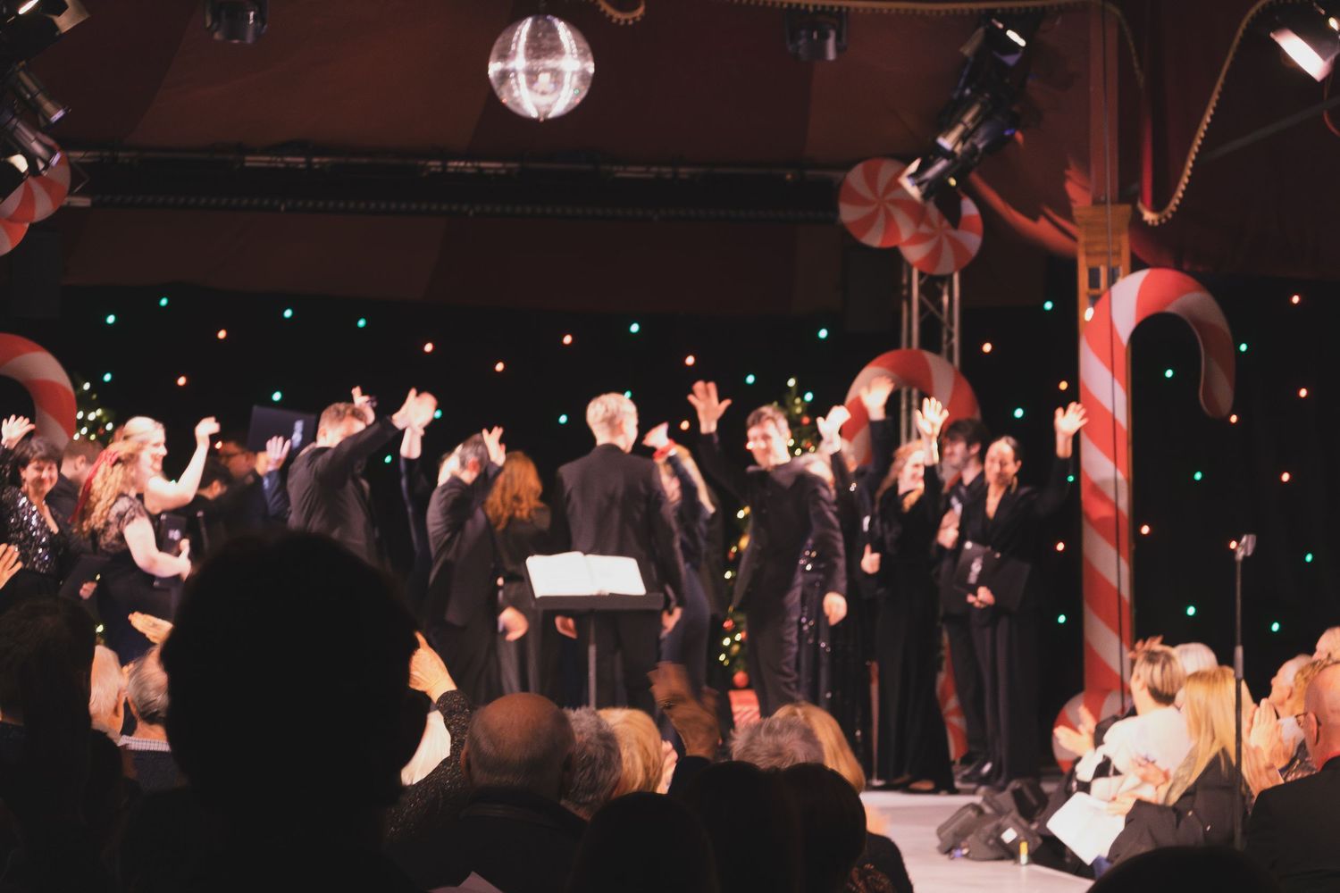 Wide shot of a choir performance with candy cane decorations and disco ball in an intimate venue.