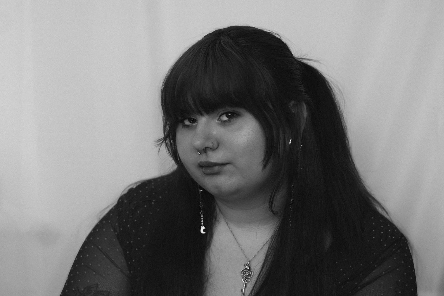 Black and white portrait of a young woman with long dark hair and bangs wearing a necklace and dark top.