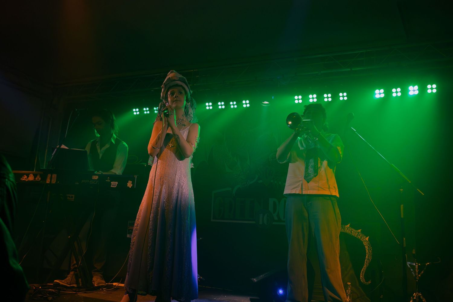 Musicians performing on stage bathed in dramatic green and blue stage lighting effects.