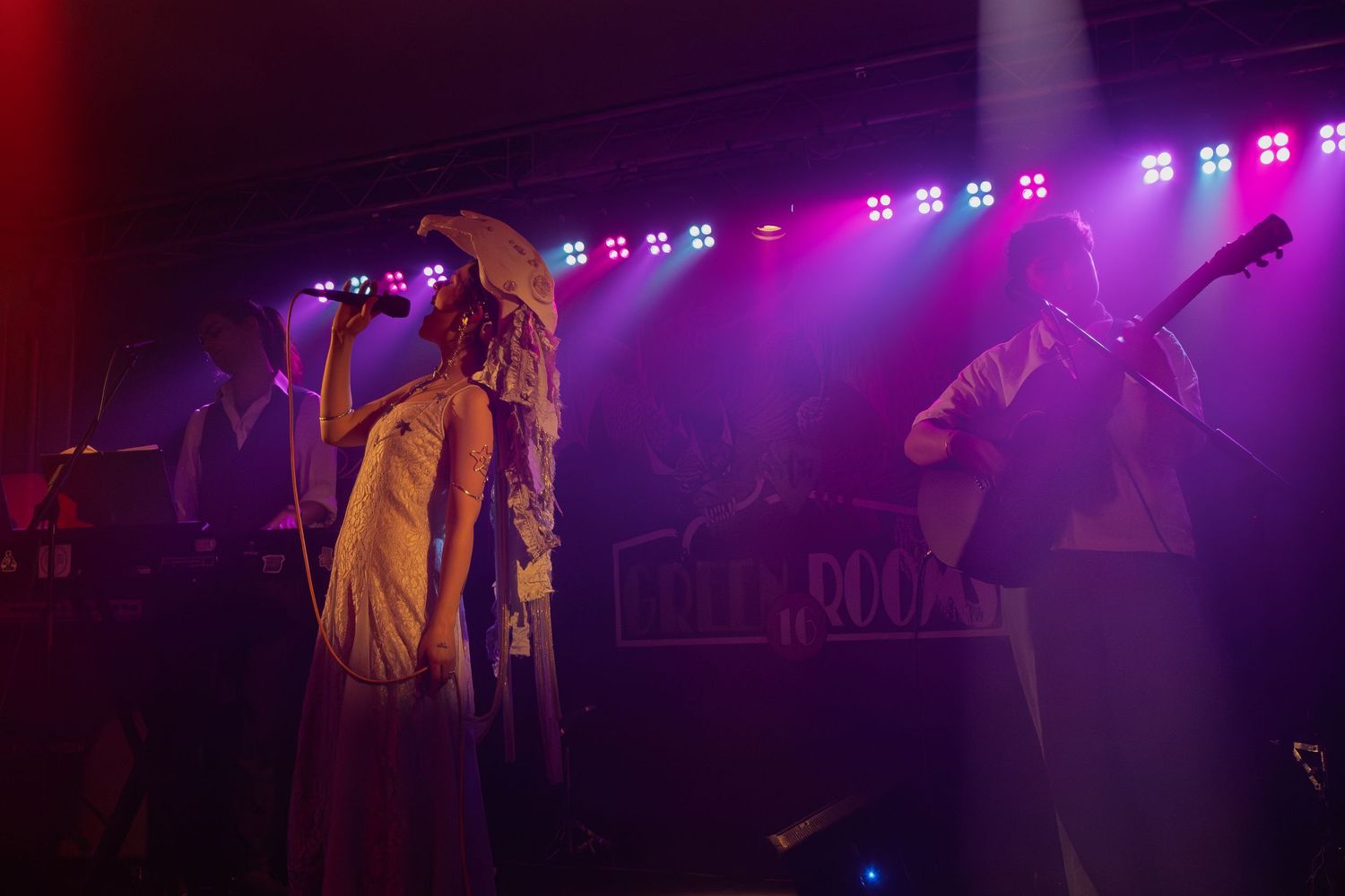 Music performance on dimly lit stage with purple and blue spotlights creating atmospheric ambiance.