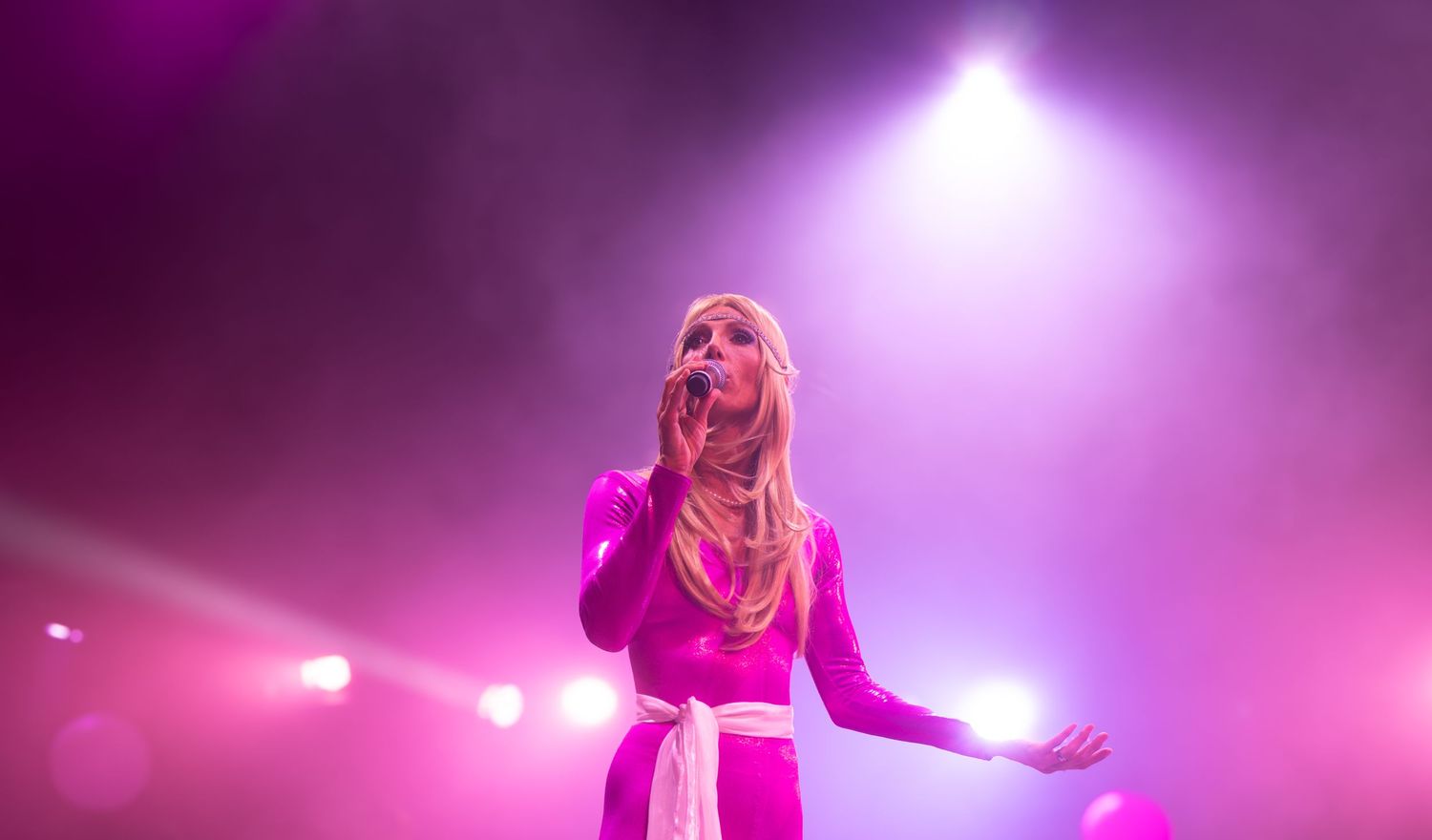 Dynamic stage performance with dramatic purple and pink lighting effects during a live concert.