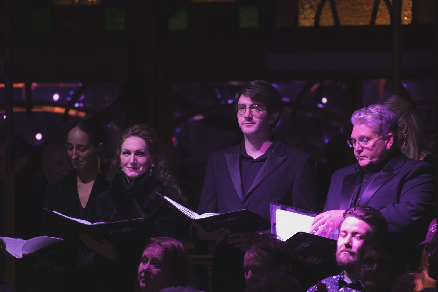 Audience members seated in a darkened theater with ambient lighting.