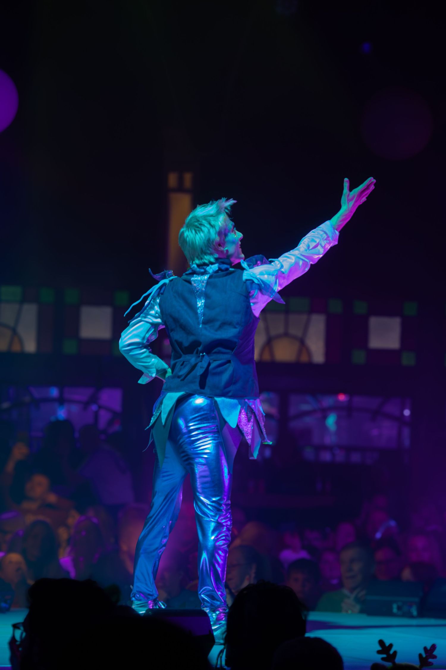 A performer in metallic blue costume strikes a dramatic pose under theatrical lighting.
