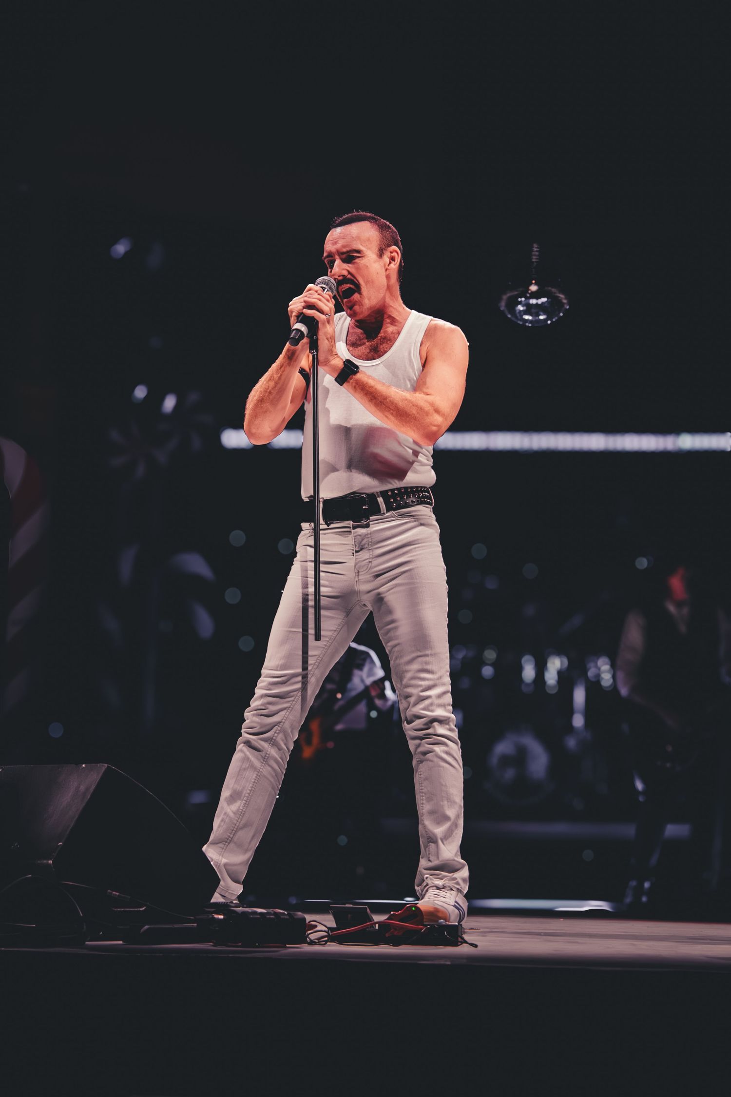 Stage performer in gray outfit singing passionately during concert performance.