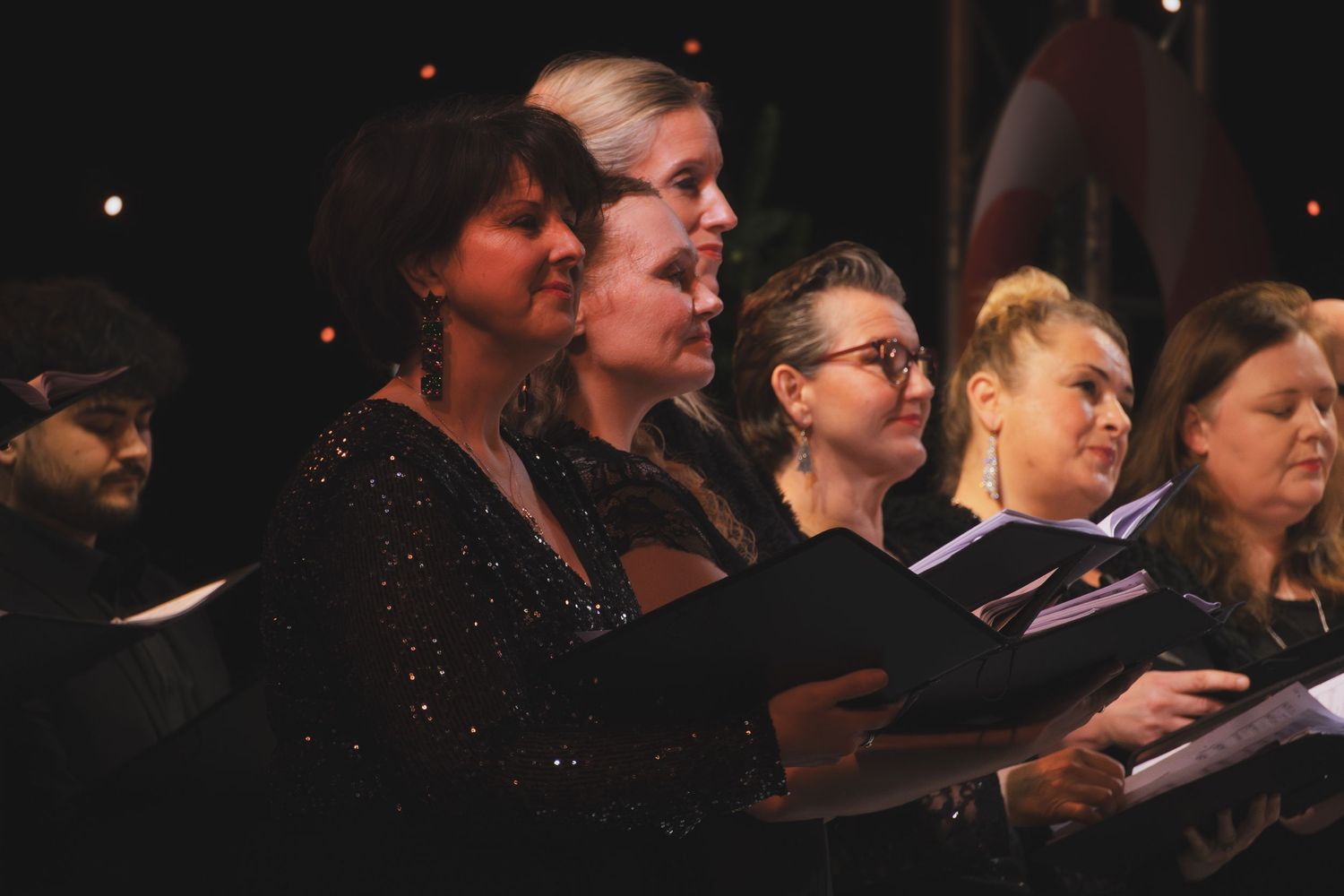 Choir members in dark attire performing during an evening concert.