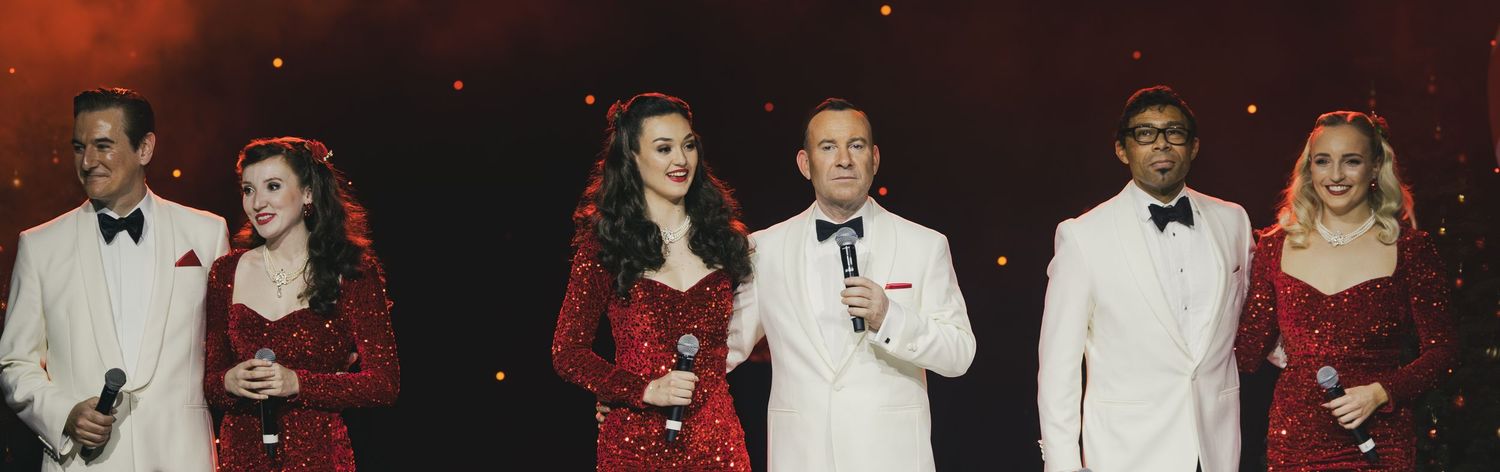 Holiday performance with dancers in red dresses and performers in formal wear on stage.