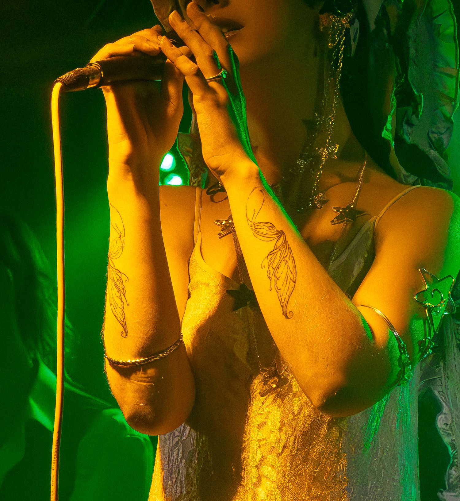 Person in dim lighting holds up camera with green ambient light creating moody atmospheric effect.