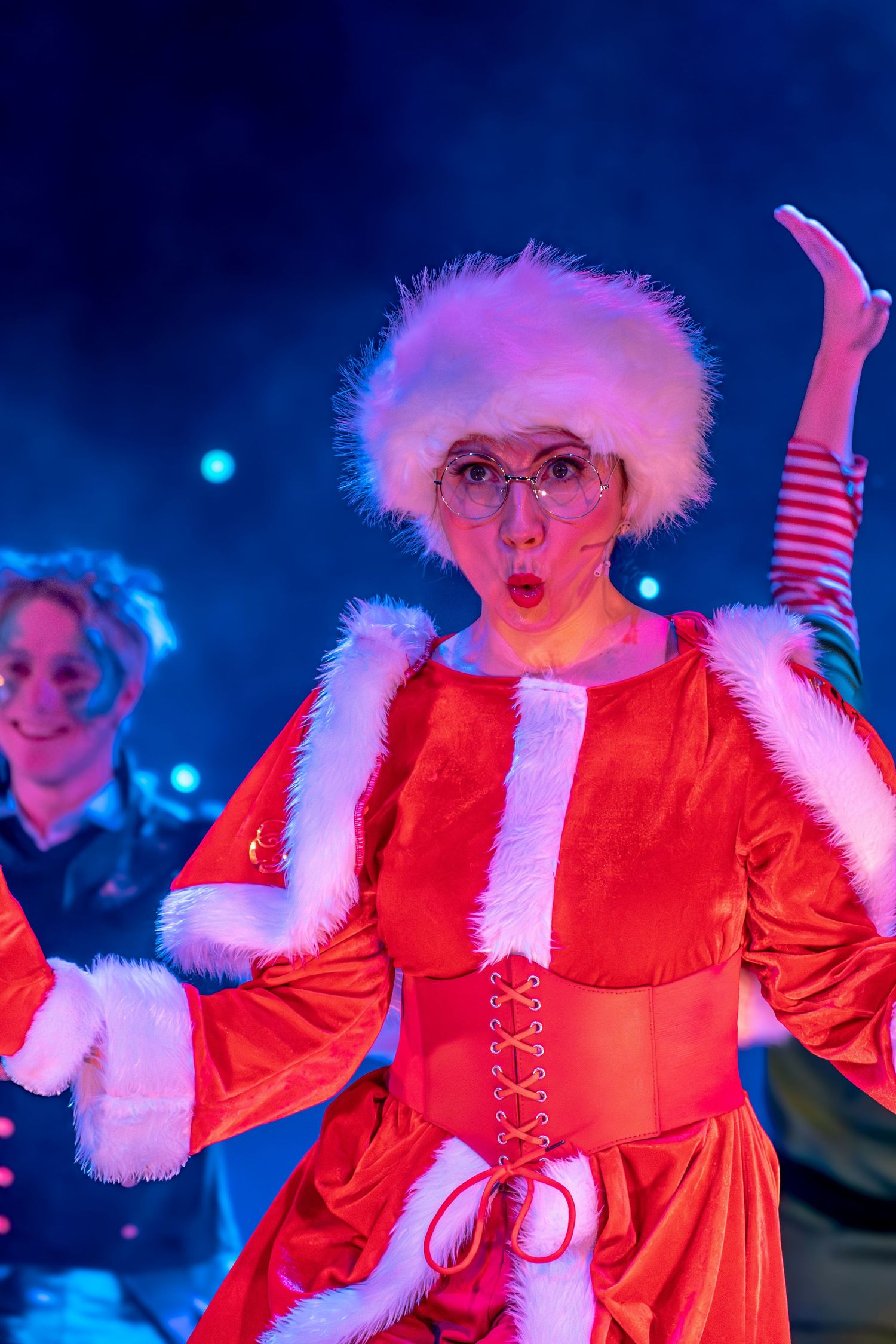 Theatrical performance featuring red-costumed character with dramatic expression under blue lights.