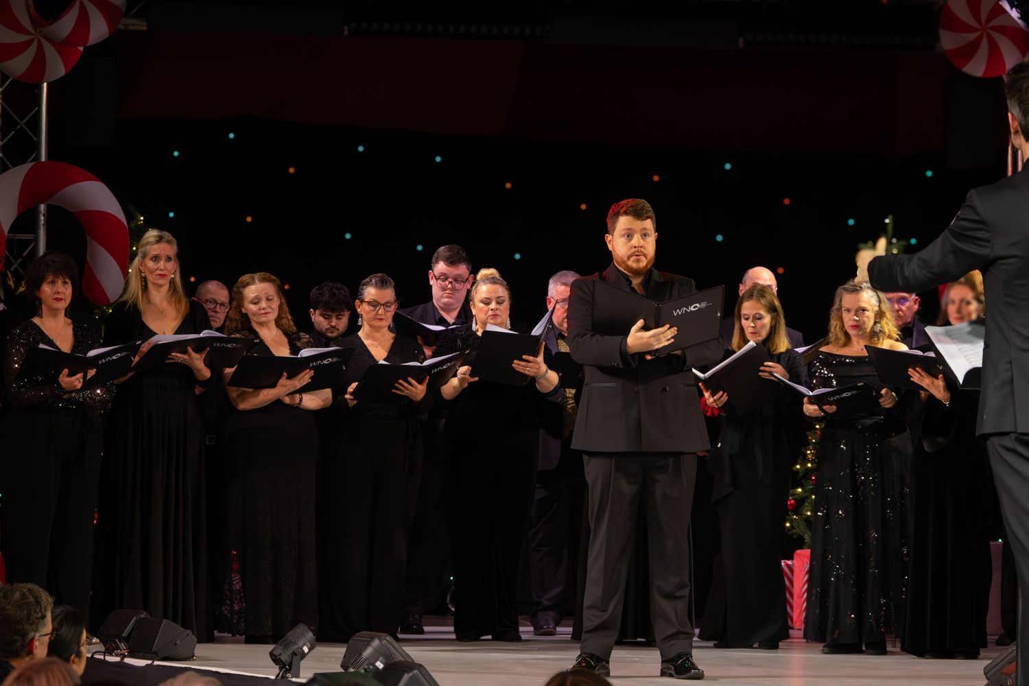 Large choir ensemble performs in formal black attire with American flag visible on stage.