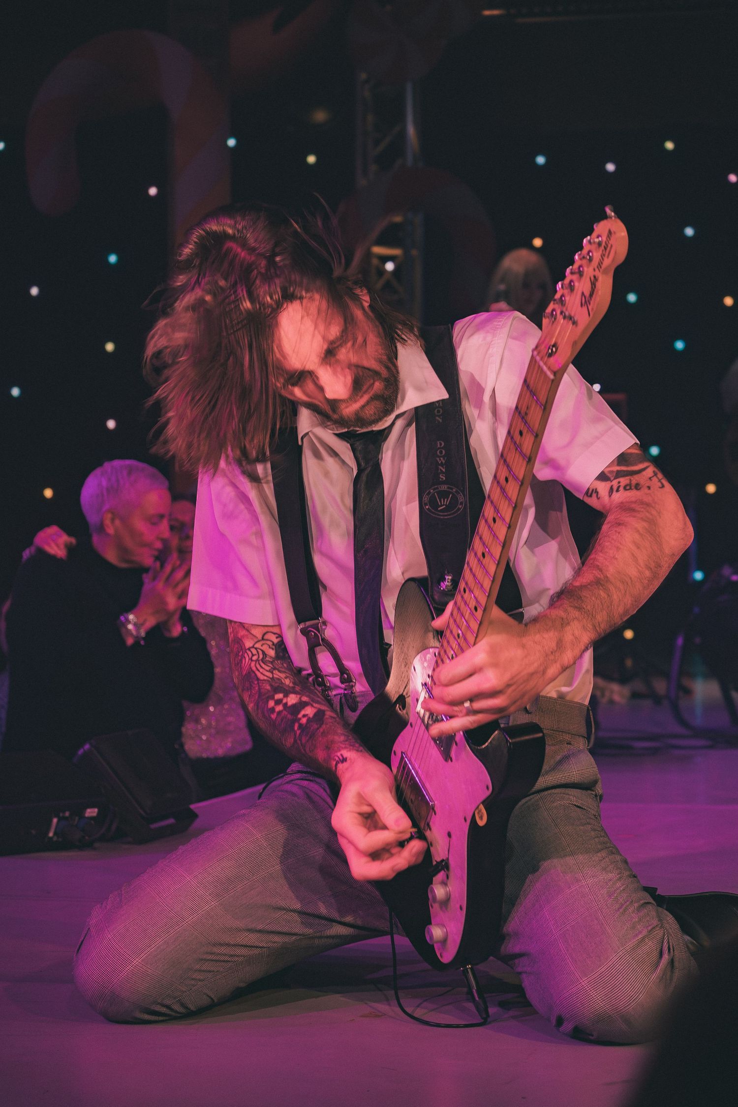Rock musicians playing guitars on stage under magenta lighting effects.