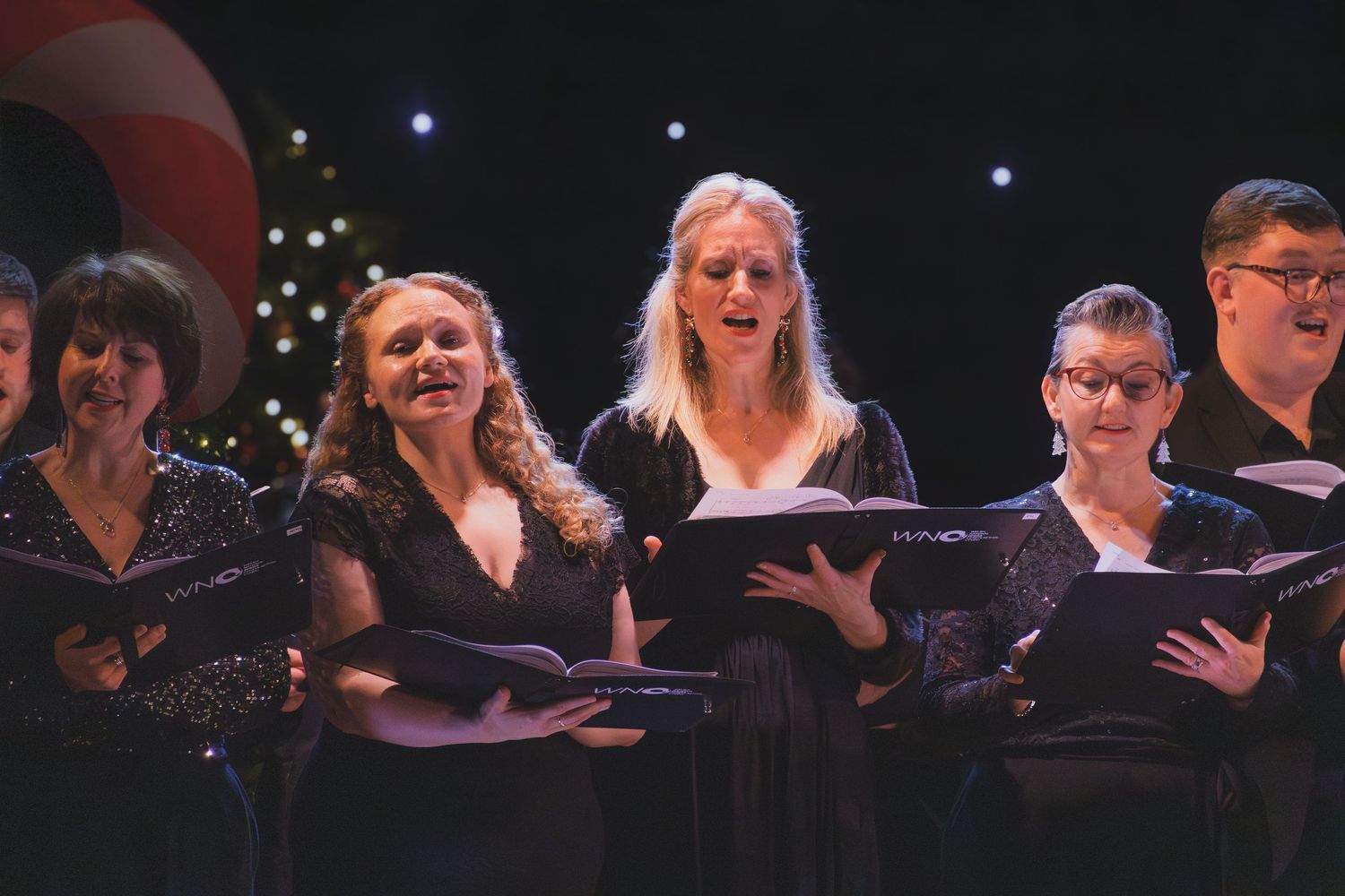 Choir performers in black attire stand together on stage during a concert performance.