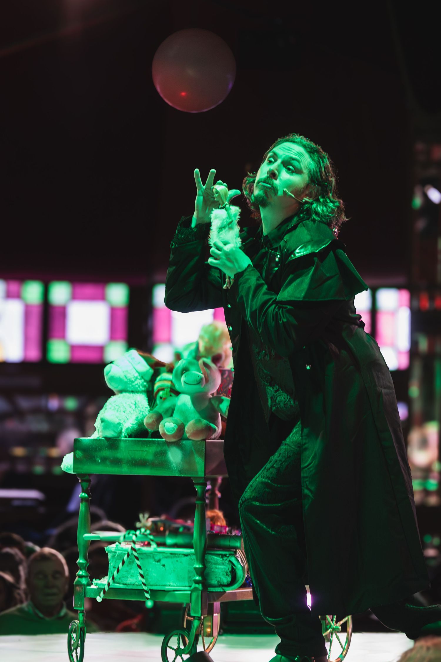 Small toy figures arranged on a cart under green theatrical lighting on a dark stage.