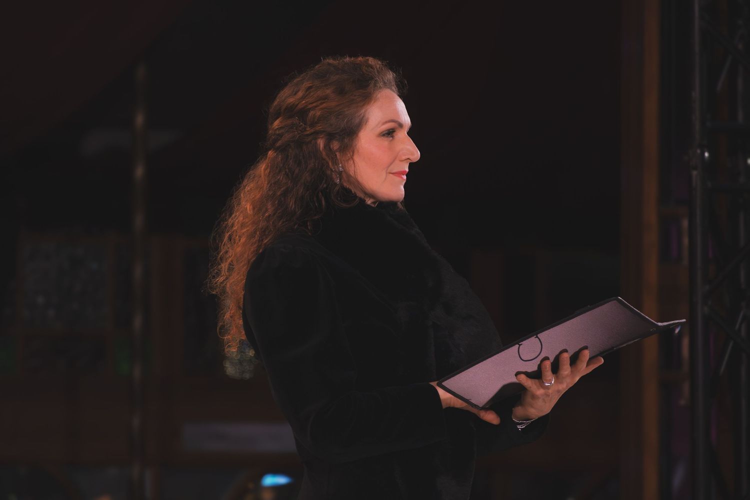 Solo performer in black holds sheet music while singing during a dramatic performance.