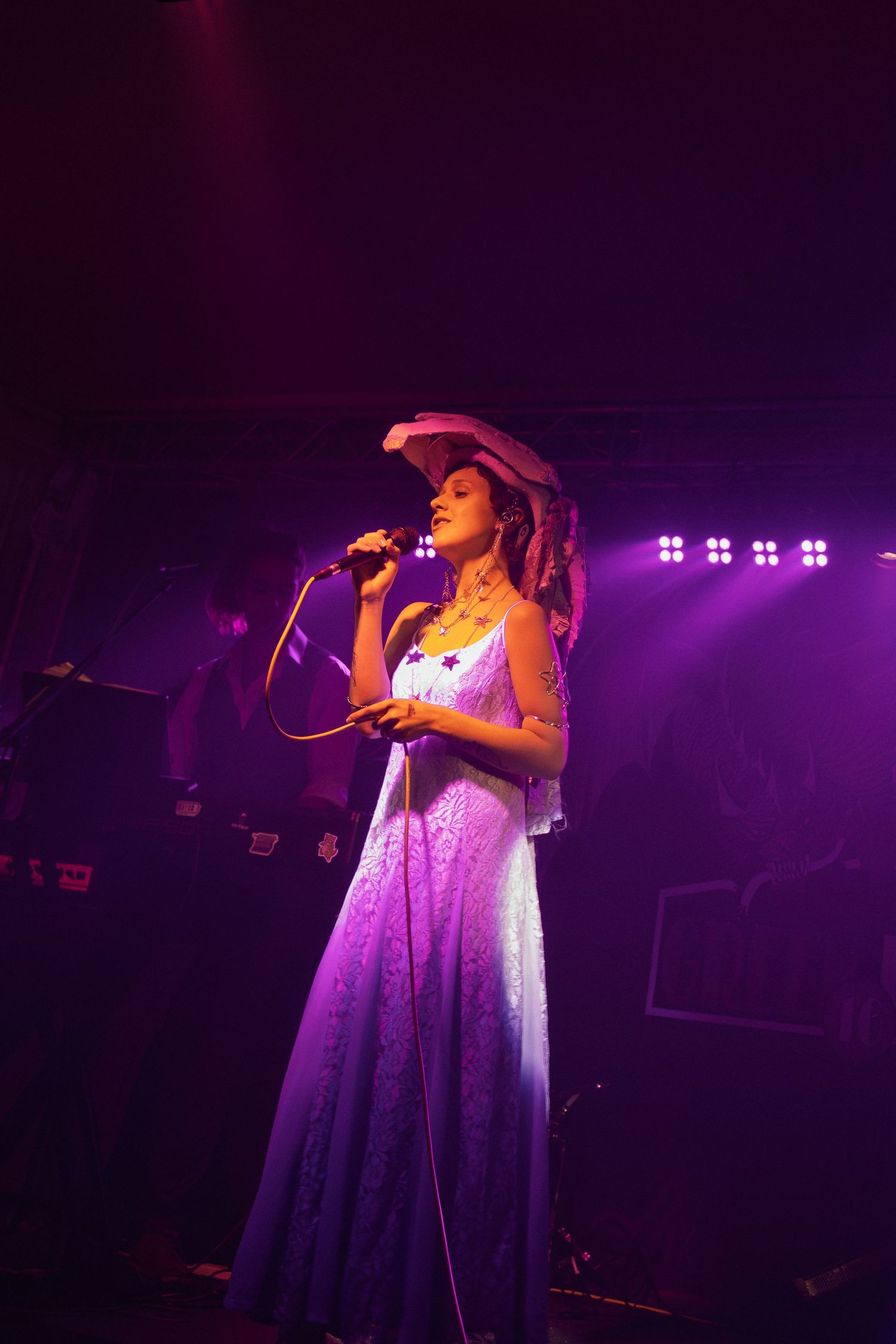 Singer performing on stage illuminated by dramatic purple and pink lighting effects during live show.