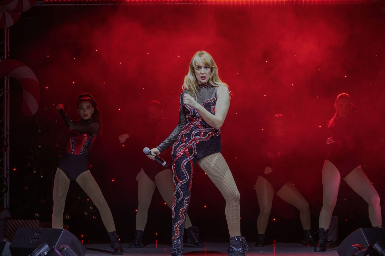 Dancers perform a choreographed routine on stage with dramatic red lighting and smoke effects.