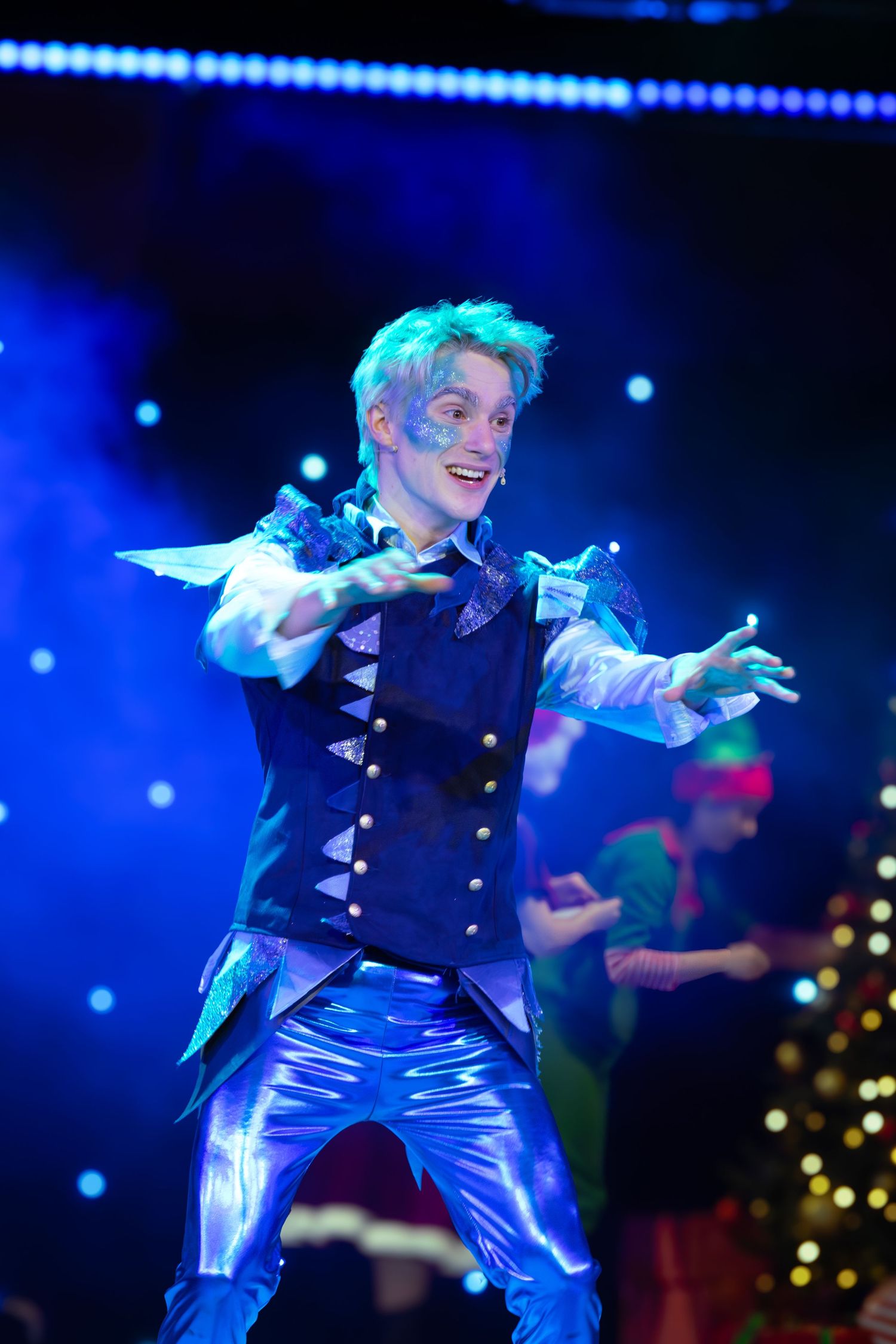 Performer in metallic pants and dark vest dances energetically under blue stage lights.