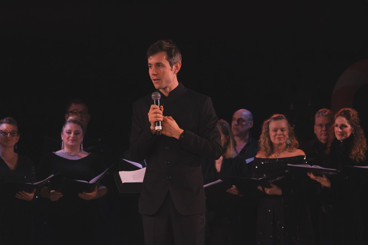 Performers on a dimly lit stage during a holiday concert with twinkling lights in the background.