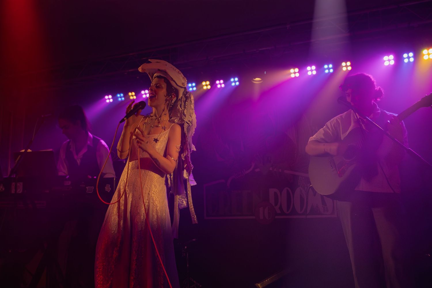 Musicians perform on stage under dramatic purple lighting during a live concert performance.