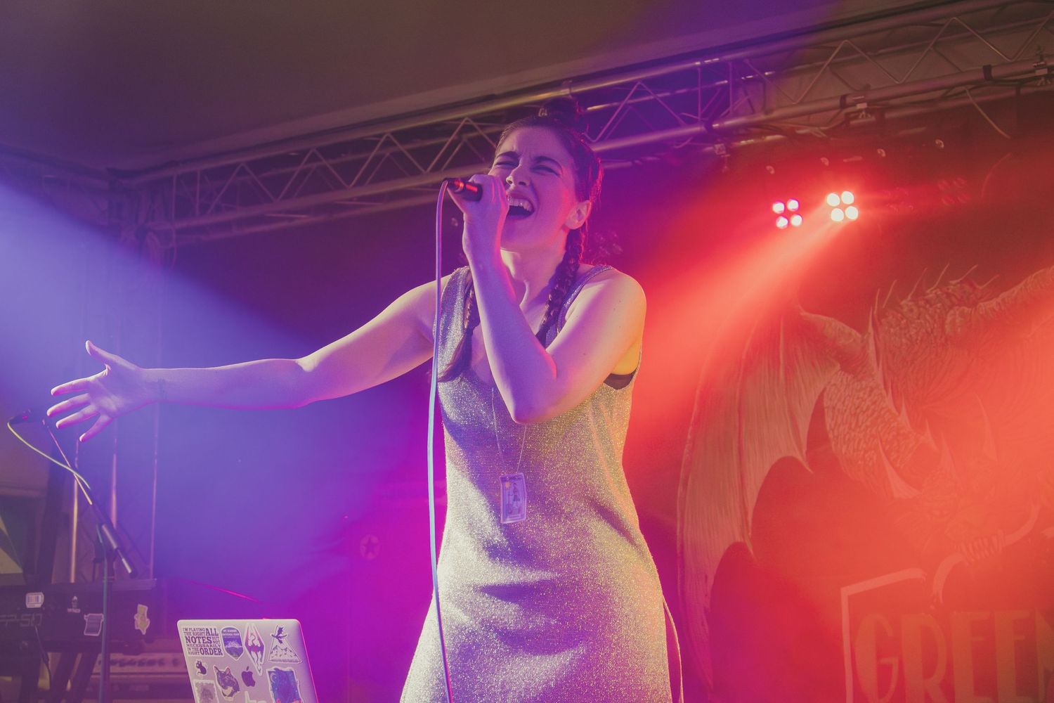 Stage performer gesturing dramatically under vibrant red and purple concert lighting.