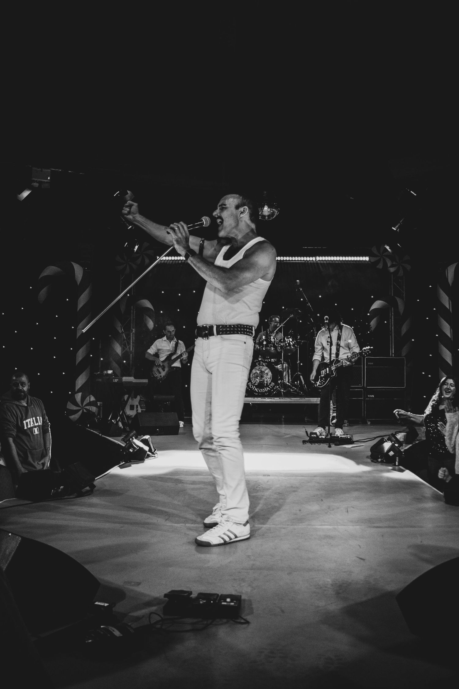Black and white concert photo showing performer on illuminated stage with crowd silhouettes.