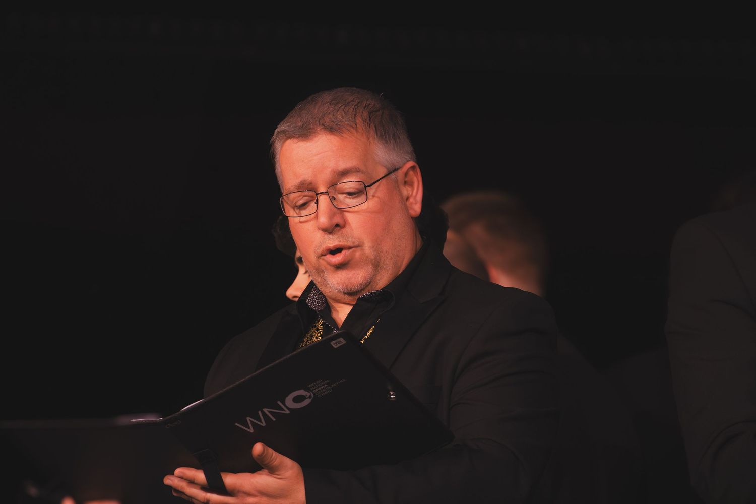 Performers reading from sheet music stand in formation during a choral concert.