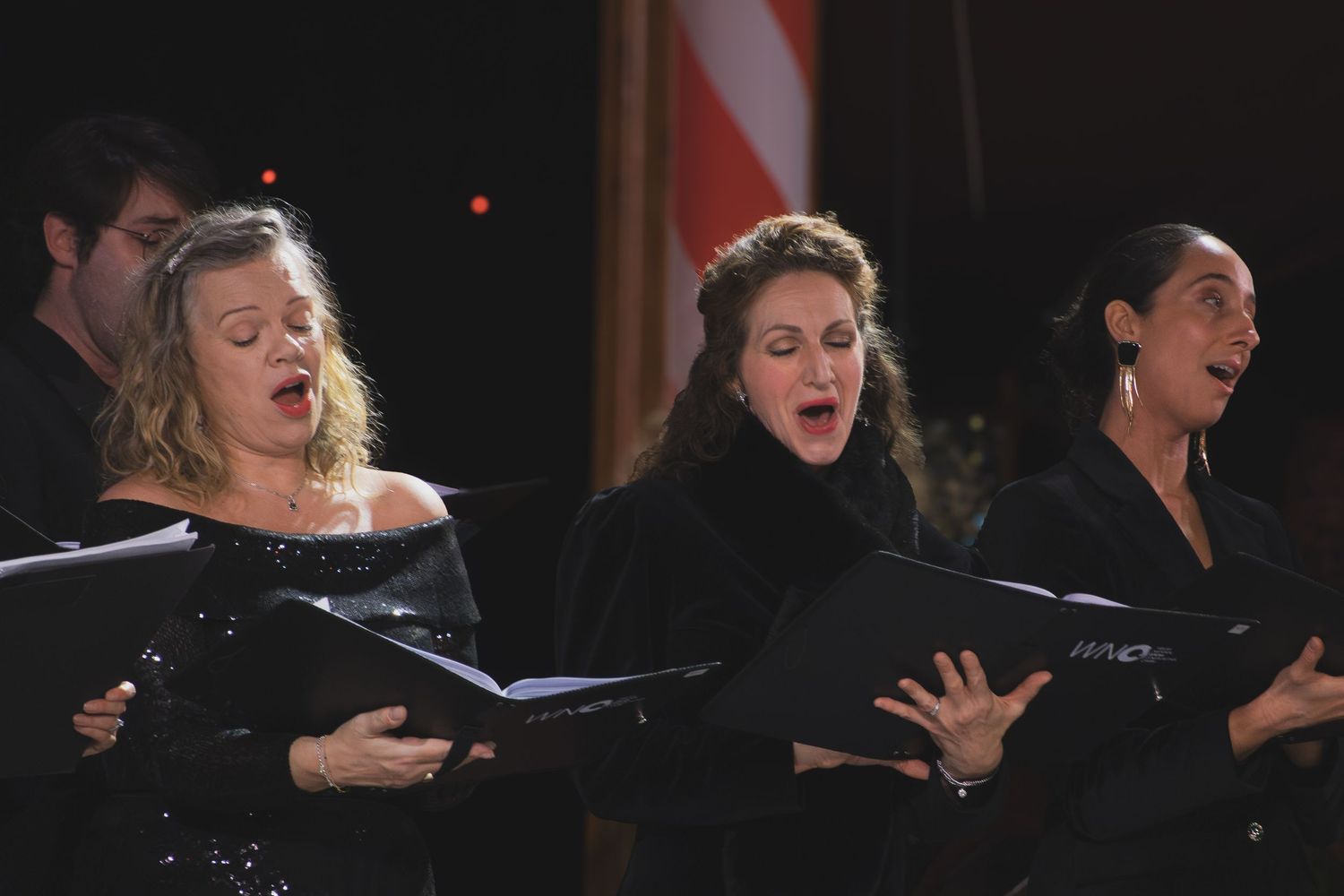 Three singers in black dresses perform passionately during a choral concert.