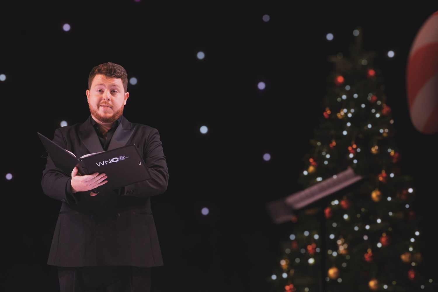 Holiday performance with decorated Christmas trees visible in the dark background.