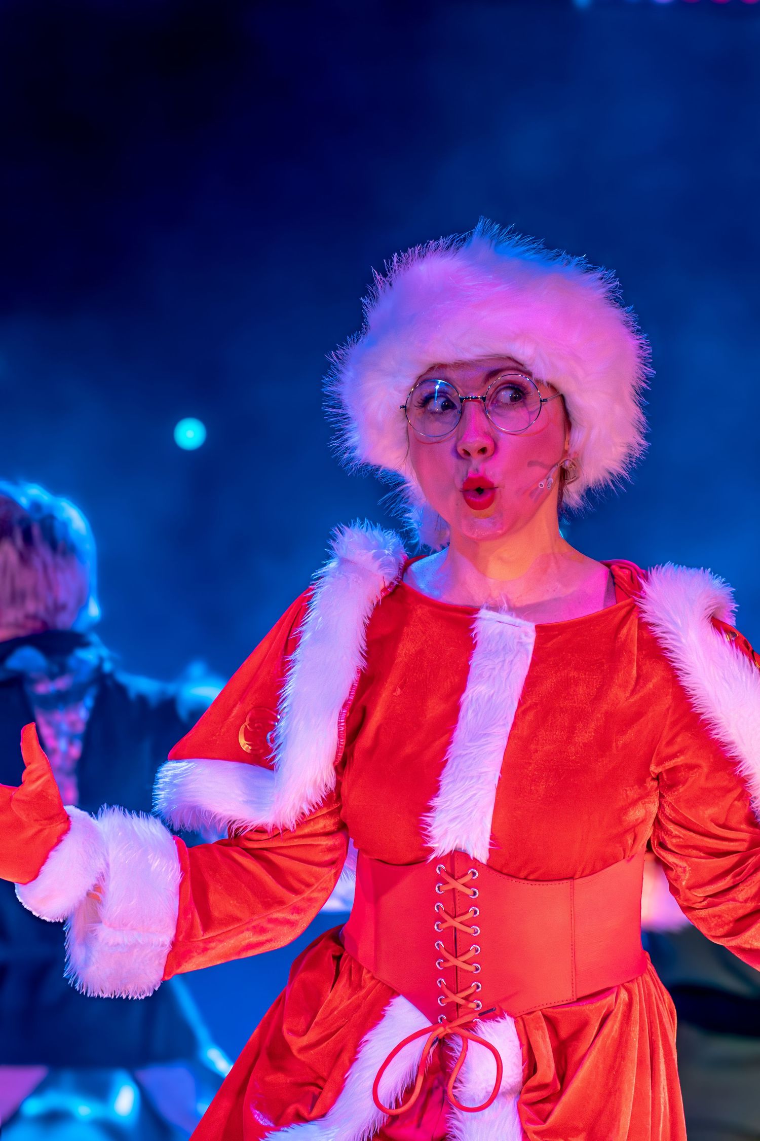 Festive performer in red costume and white fur trim expressing joy during stage show.