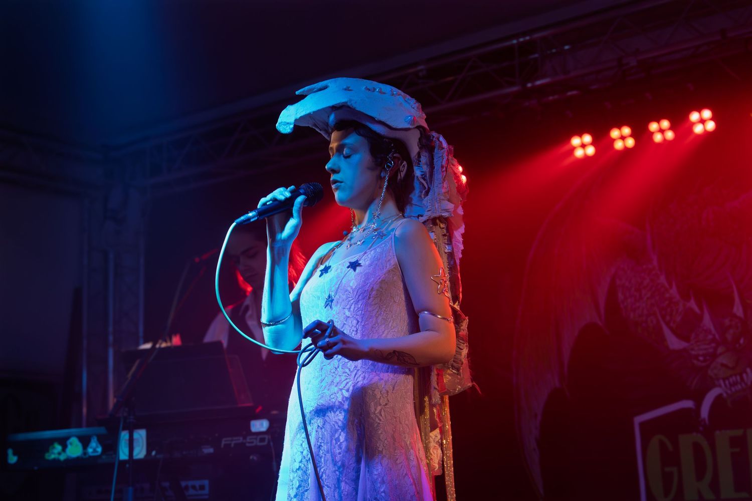 A singer performs on stage in a flowing dress under blue and red stage lights.