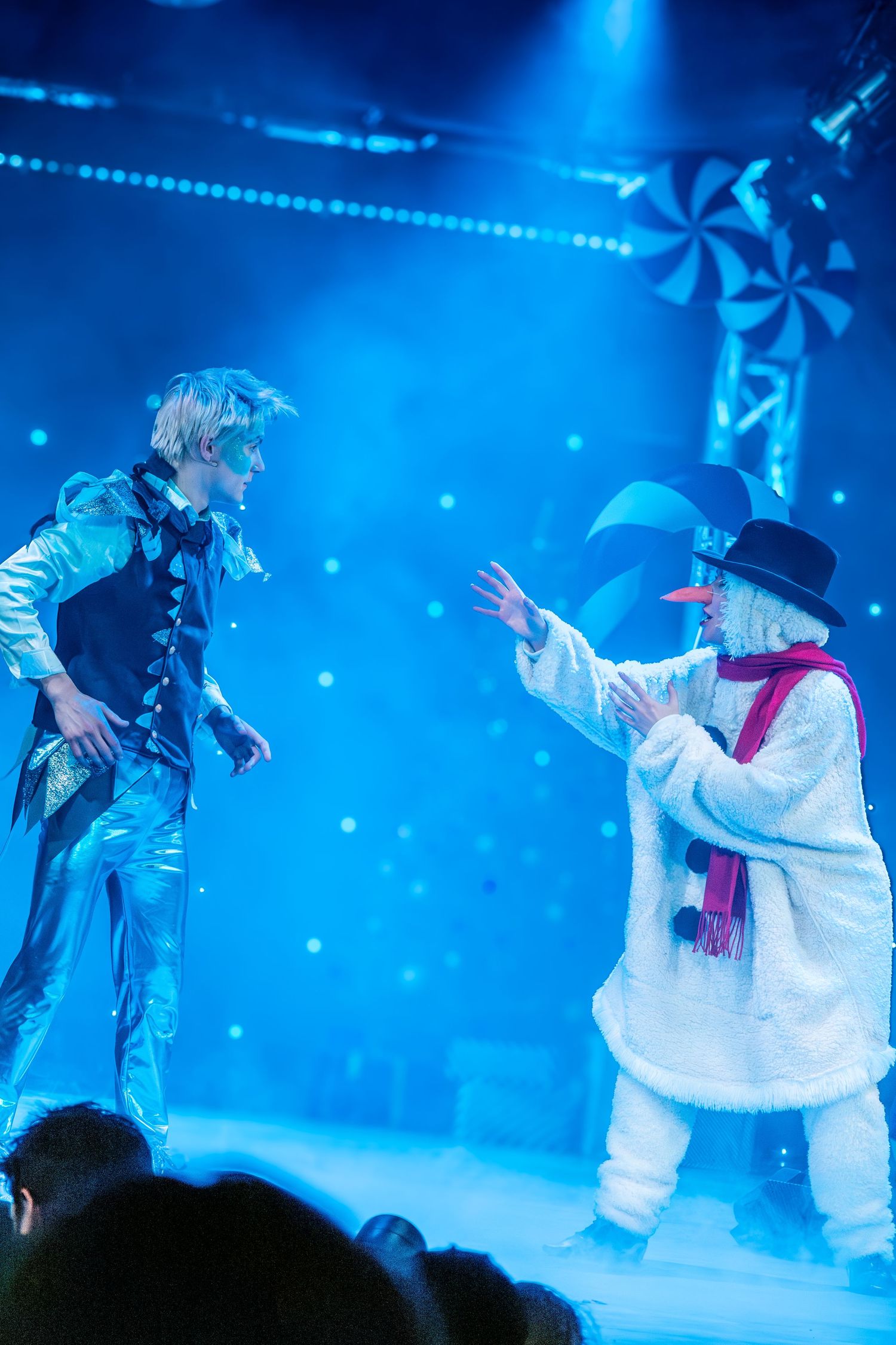 Performers in white costumes dance under dramatic blue stage lighting during a theatrical show.